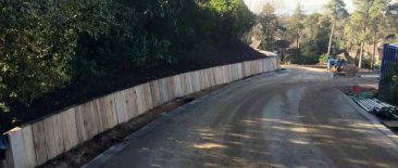 Curved gabion retaining wall made of wire‑mesh baskets filled with stone, installed beside a newly surfaced curved roadway at Lynwood, Camberley