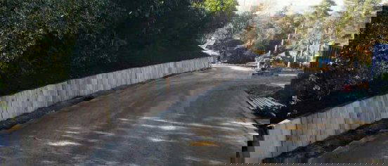 Curved gabion retaining wall made of wire‑mesh baskets filled with stone, installed beside a newly surfaced curved roadway at Lynwood, Camberley