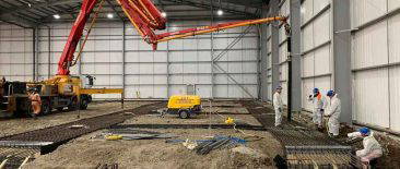 Heavy-duty excavators and rebar reinforcement being installed within an industrial warehouse shell at Edmonton bulk‑excavation project