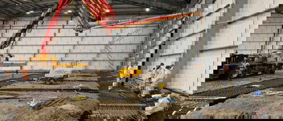 Heavy-duty excavators and rebar reinforcement being installed within an industrial warehouse shell at Edmonton bulk‑excavation project
