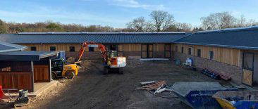 Tracked excavator digging foundation trenches at Langshot Stud equestrian facility in Surrey