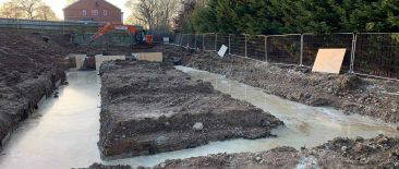 Freshly poured concrete infill within foundation trenches on a construction site at Bracknell, surrounded by excavated soil and temporary fencing