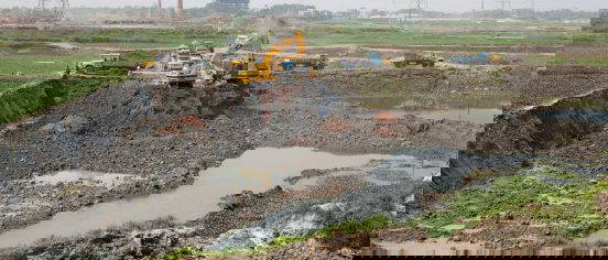 Excavator and dump trucks working on large construction excavation site