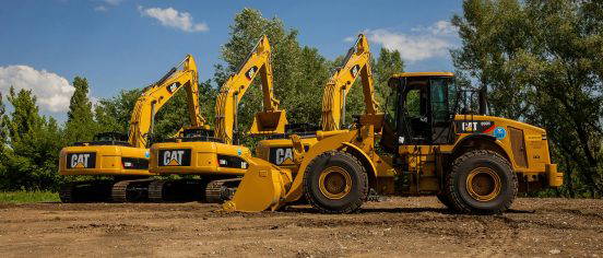 Yellow CAT construction machinery including excavators and a wheel loader parked on a dirt worksite under a blue sky